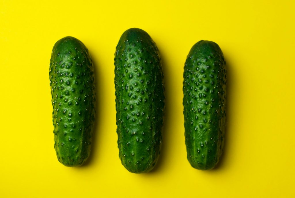 A stock photo of three cucumbers on a yellow surface.