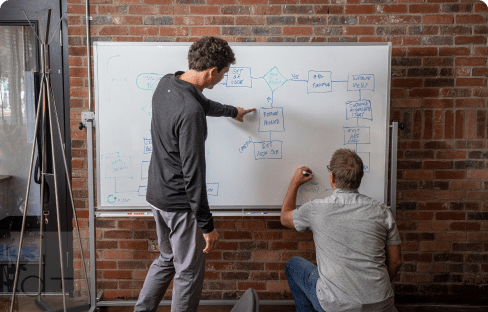 Two men creating a flow chart on a whiteboard, representing our commitment to innovative and effective strategy and product development.