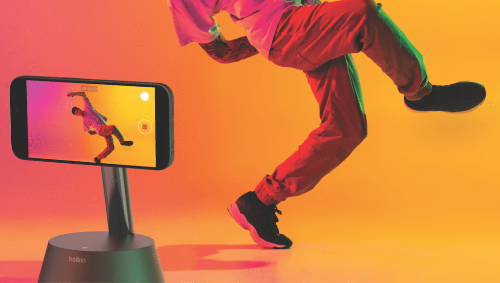 Man dancing in the background. In the foreground is a device with a phone in it recording his dancing.
