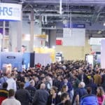 A bustling crowd at CES 2025 featuring tech booths, including Hirose Electric Co. and Mirobot, showcasing innovative technologies.