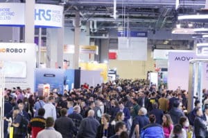 A bustling crowd at CES 2025 featuring tech booths, including Hirose Electric Co. and Mirobot, showcasing innovative technologies.