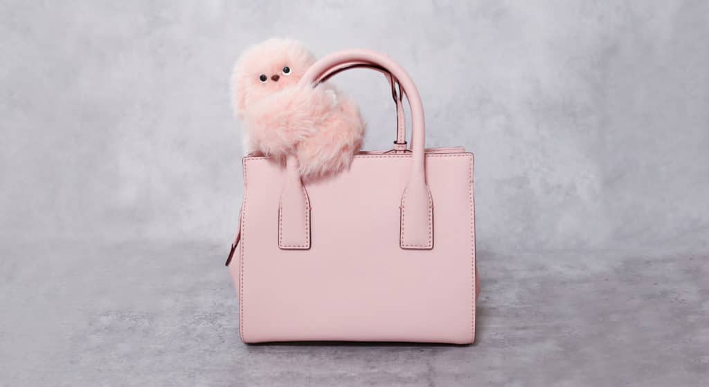 Mirumi, the shy robot companion, nestled on a stylish pink handbag, blending adorable robotics with everyday fashion.